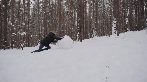 Smiling Caucasian Man with Effort Rolls Large Snow Globe Uphill