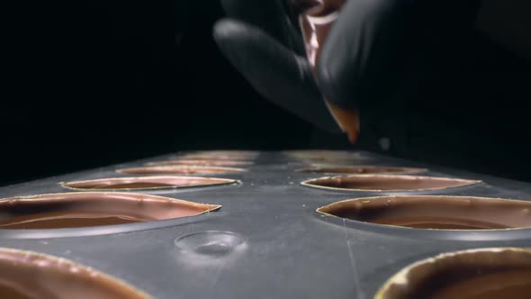 Chocolatier Fills Chocolate Molds with Liquid Chocolate Filling for Praline Sweets , Making of