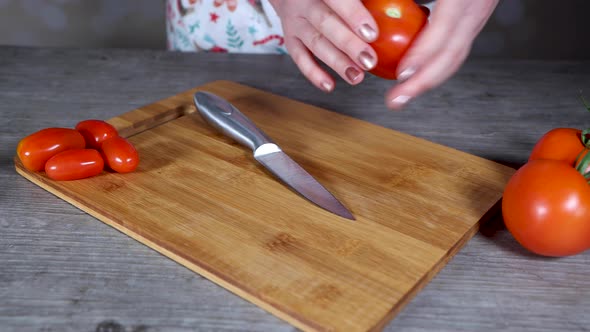 A woman in a kitchen cutting up a large red tomato on a chopping board