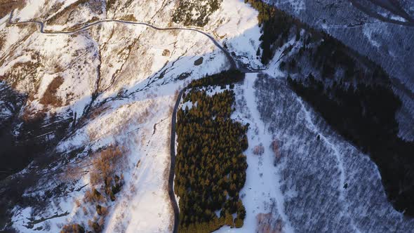 Scenic Top Aerial View of Snow Covered Forest and Curved Highway During sunset.Road Across Mountain