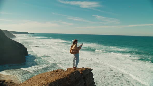 Woman Stand on Edge of Ocean Cliff with Phone