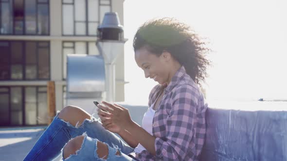 Fashionable young woman on urban rooftop using smartphone