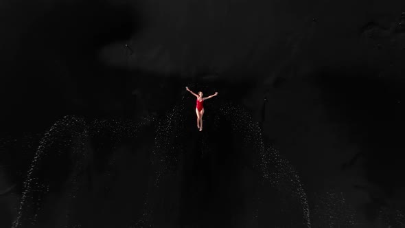 Top View of a Caucasian Woman in a Red One Piece Swimsuit Lying on a Black Beach