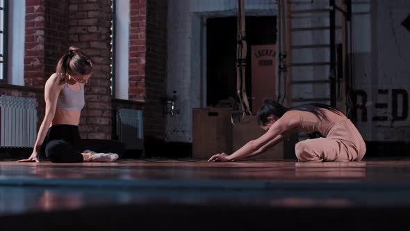 Two Skinny Women Training Together in the Gym  Doing Stretching Exercises