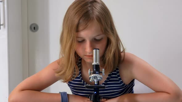 Cute Blond Teenage Girl in a Striped Shirt is Looking Through the Microscope