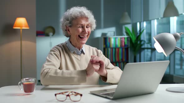 Happy Elderly Woman Using Laptop and Smiling Sitting in Spacious Living Room at Home