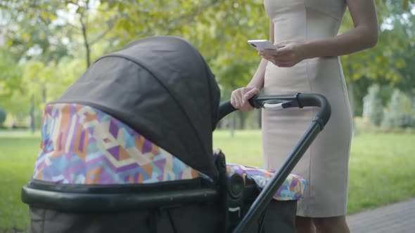 Unrecognizable Slim Caucasian Young Mother in Elegant Dress Standing with Baby Stroller in Summer