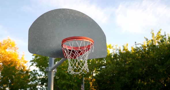 Sliding left shot of a basketball hoop with a metal backboard, orange rim and net in an empty park c