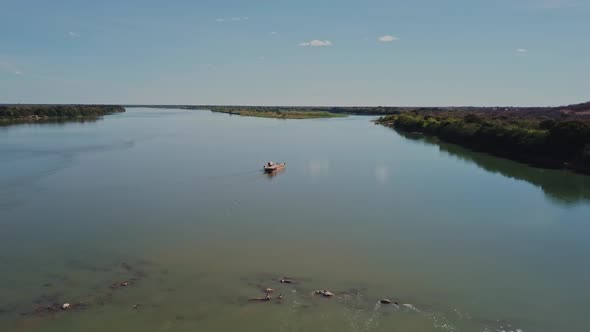 Wide aerial shot following a small ferry sailing on the Sao Francisco River in rural Brazil.