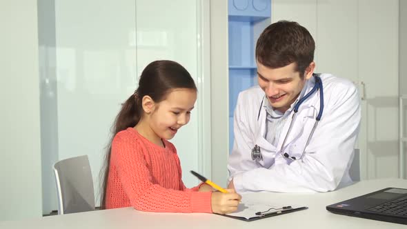 Little Girl Draws on Clipboard Near the Doctor