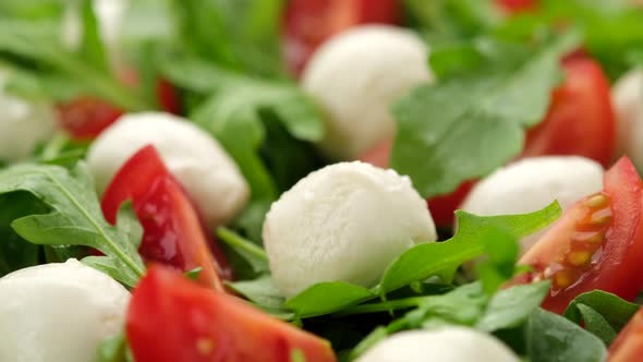 Pour olive oil on caprese salad with mini mozzarella, tomatoes cherry and arugula