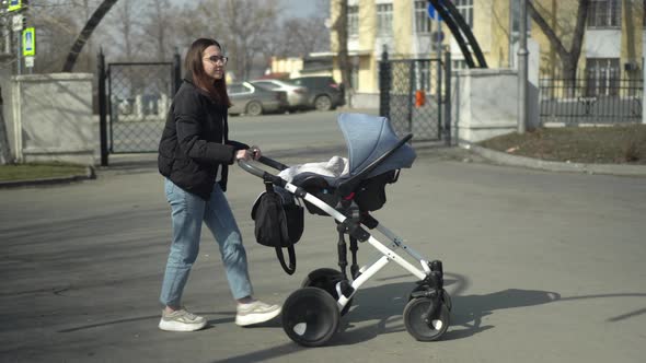 A Young Mother Walks on the Street with a Baby in a Stroller
