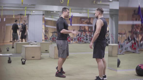 Wide Shot of Two Body-builders Talking in Gym. Strong Caucasian Sportsmen Standing in Sports Club