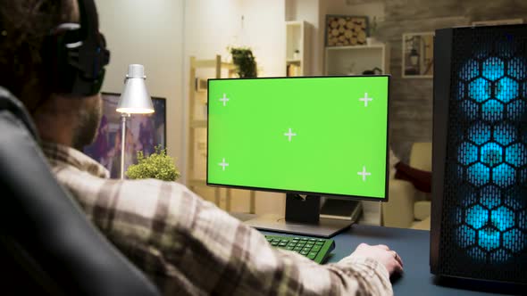 Man with Headphones Playing Games on Computer with Green Screen