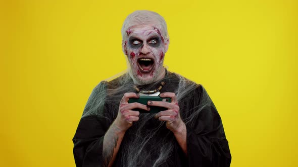 Sinister Man Halloween Zombie Enthusiastically Playing Racing Drive Video Games on Mobile Phone