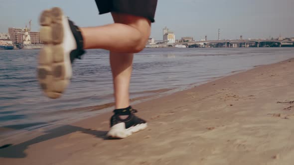 Muscular Young Man Running on the Beach in the City on a Sunny Day