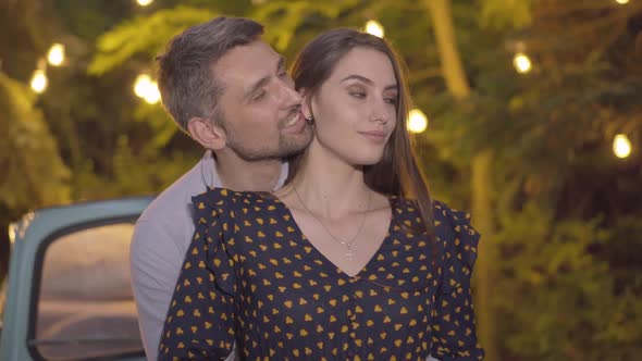 Portrait of Loving Couple Hugging with Garland Lights at the Background. Romantic Caucasian