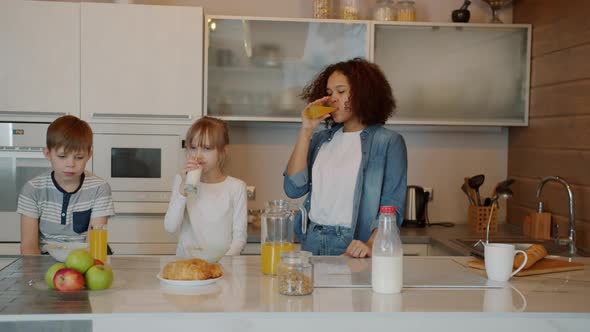 Sleepy Children and Babysitter Having Breakfast in Kitchen Cereal Milk and Juice