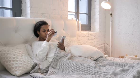 Online Shopping Via Smartphone By Young African Girl Relaxing in Bed