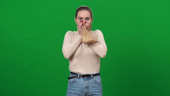 Panicked Woman Breathing in Paper Bag Looking at Camera in Green Screen