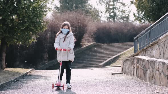 The Girl in a Protective Mask Is Driving a Scooter in a Park