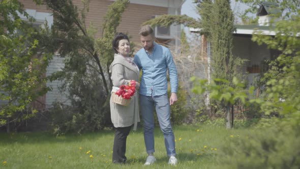 Portrait Mature Woman with the Basket with Tulips in Hands Talking with Her Grandson on the Backyard