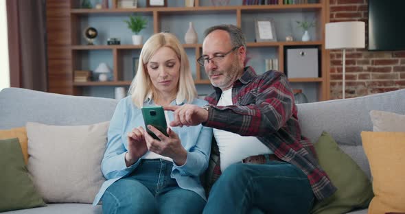 Mature Couple at Home Using Smart Phone Together and Smiling.