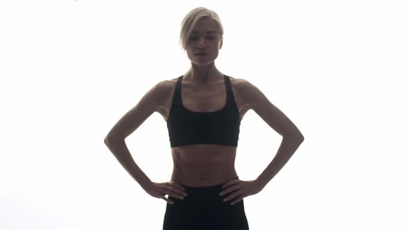 Sporty Woman with Raised Body in Tracksuit Stands Against White Background in Studio and Sighs