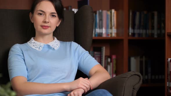 Portrait of Smiling Beautiful Pretty Woman Sitting in a Chair in Library Office Bookshelf Background