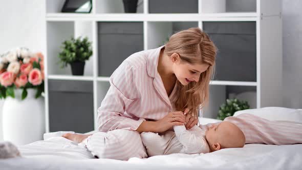Joyful Mother Playing with Cute Baby Sitting on Bed at Cozy White Room