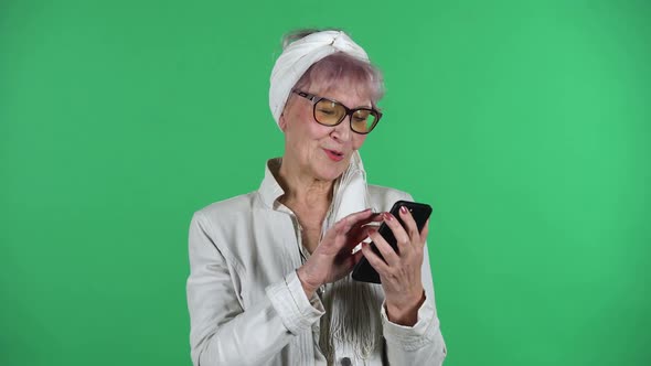 Portrait of Old Stylish Woman Is Texting on Her Phone Isolated Over Green Background
