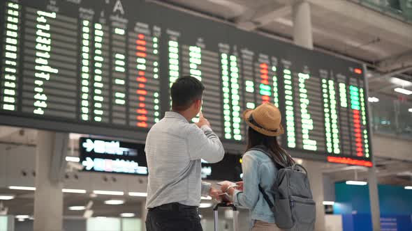 Couple Asian people checking on flight schedule board in airport terminal.