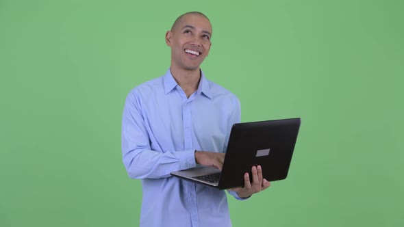 Happy Bald Multi Ethnic Businessman Thinking and Talking While Using Laptop