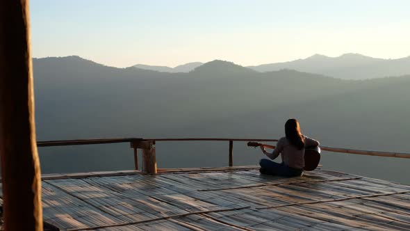 Rear view of a female sitting and playing guitar on wooden balcony