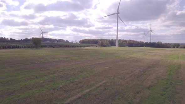 Flying low over field and farmland.  Camera moves towards wind turbine with other windmills in backg