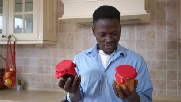 Portrait of Satisfied African American Man Stretching Jars with Jam Smiling Looking at Camera