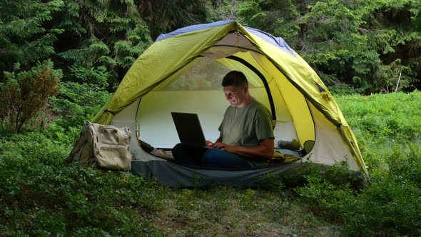 A Man Works on a Laptop in a Tourist Camp in a Beautiful Forest