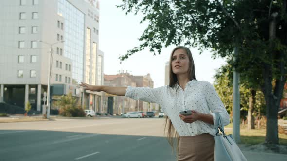 Slow Motion Portrait of Lady Hailing Taxi Looking at Smartphone Screen in a Hurry in Urban Street