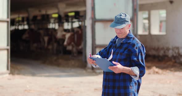 Farmer Analyzing and Writing on Clipboard Against Cowshed