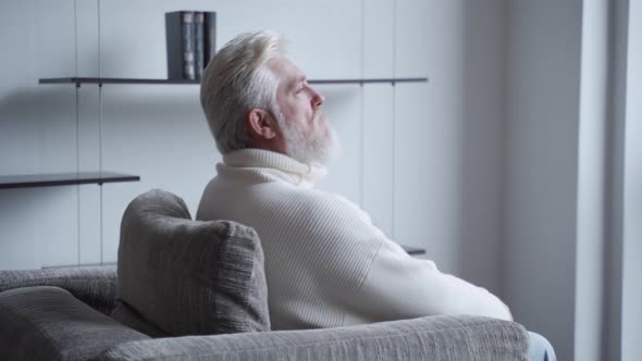 Relaxed Mature Man with a Gray Beard at Home Sitting in a Chair