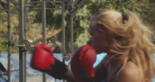 Woman Punching Bag In Boxing Gloves In Outdoor Gym