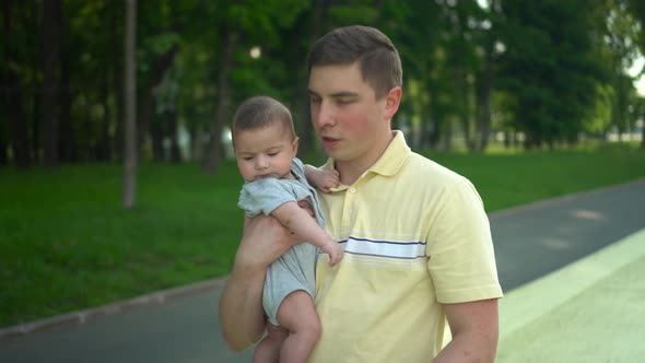 A Young Dad Carries His Son in His Arms and Kisses Him