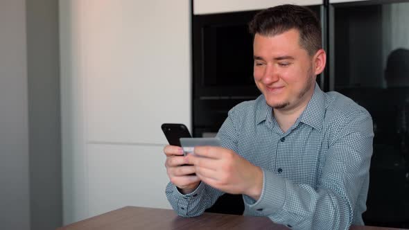 Portrait of Caucasian 30s man shopping online with smartphone and credit card at home indoors