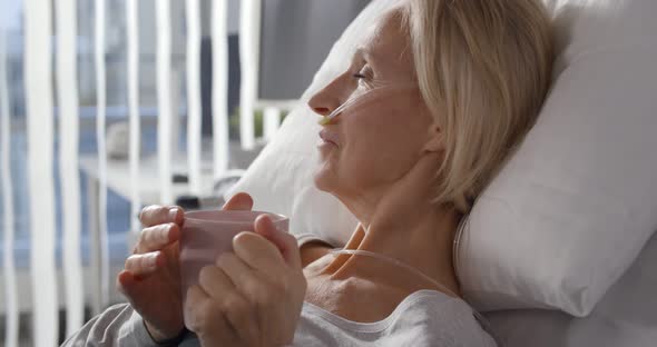 Portrait of Sick Aged Woman Patient with Breathing Tube Drinking Water in Mug