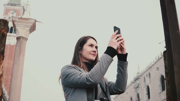 Happy Attractive Caucasian Female Tourist Taking Smartphone Photos of Ancient Buildings in Old Town