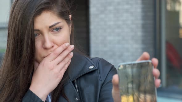 Upset Woman Looks at a Smartphone and Shows His Broken Screen.