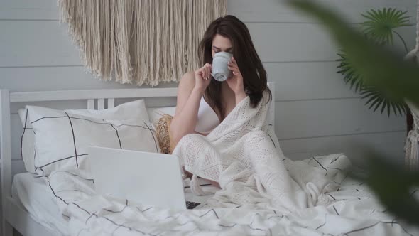 Girl Was Wrapped in a Blanket, Drinking Coffee and Using a Laptop While Sitting on the Bed