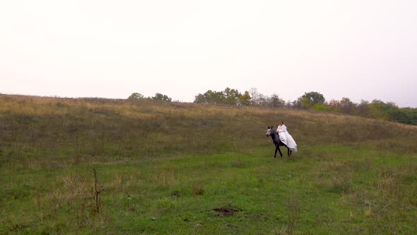 Long-haired Female in White Dress Is Riding Horse Along Wood