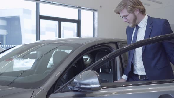 Handsome Bearded Businessman in Glasses and Business Suit Gets in the Car. Car Dealership.