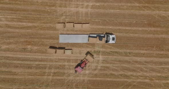 Tractor loading Hay bales onto a trailer, Aerial view.